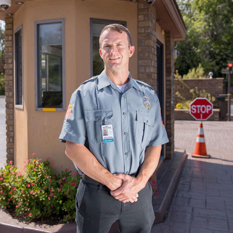 Security guard from Elite Security & Staffing standing in front of a checkpoint gate at a private property entrance.